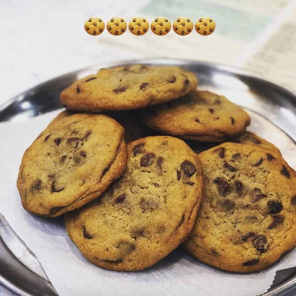 A metal tray filled with freshly baked chocolate chip cookies on a white paper liner.