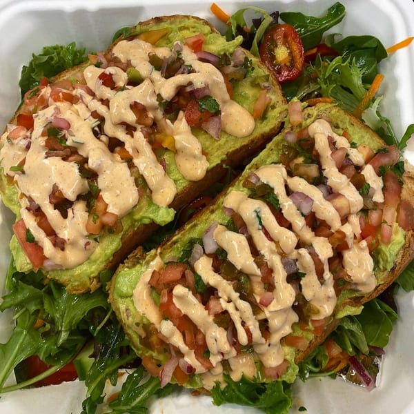 Two avocado toasts topped with pico de gallo and a creamy sauce, served with a side salad.