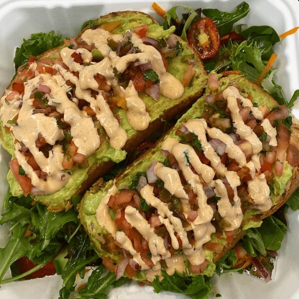 Two avocado toasts with pico de gallo and a creamy sauce, served with a side salad.
