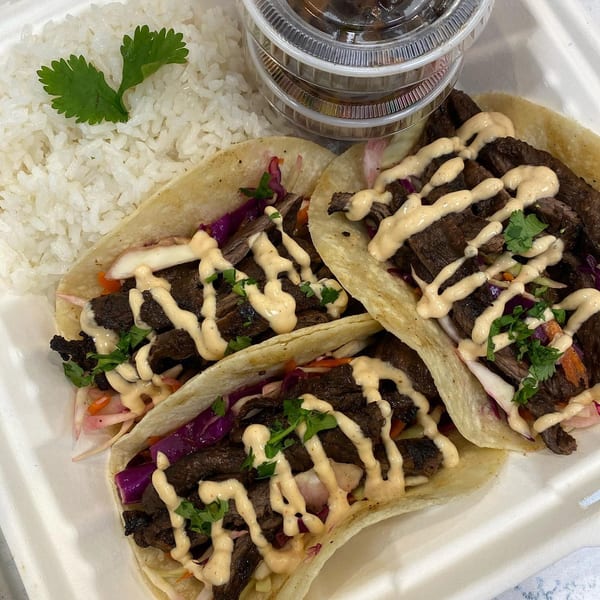 Three Emma's Deli tacos with meat, cabbage, sauce, cilantro, and a side of white rice.
