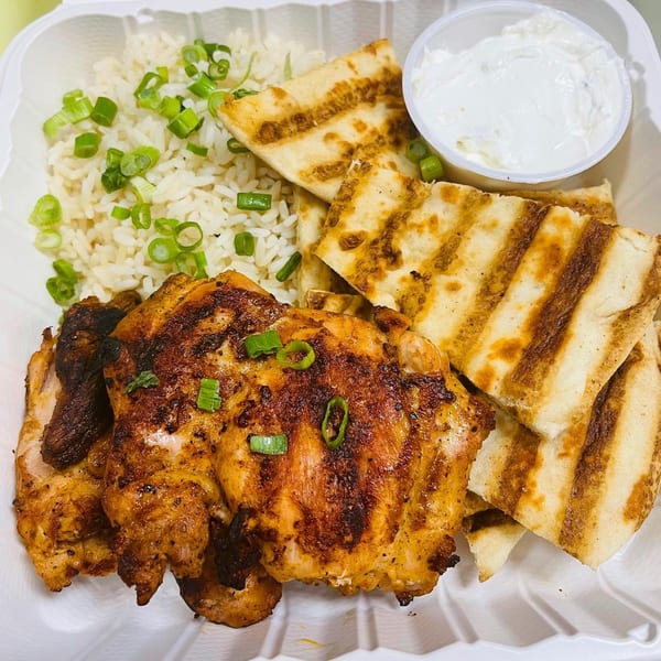 Grilled chicken, rice with green onions, pita bread, and a side of white sauce in a deli container.