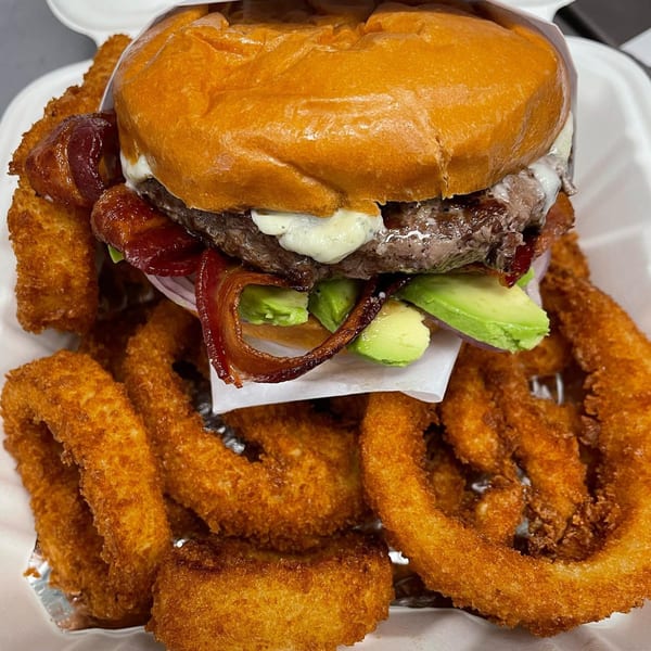 A deli burger with bacon, avocado, and melted cheese, served with crispy onion rings.