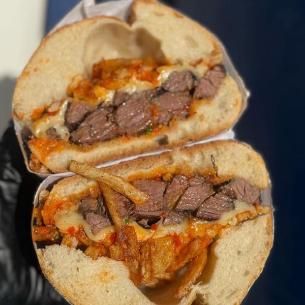 A sliced Emma's Deli steak sandwich with melted cheese, sauce, and fries inside.