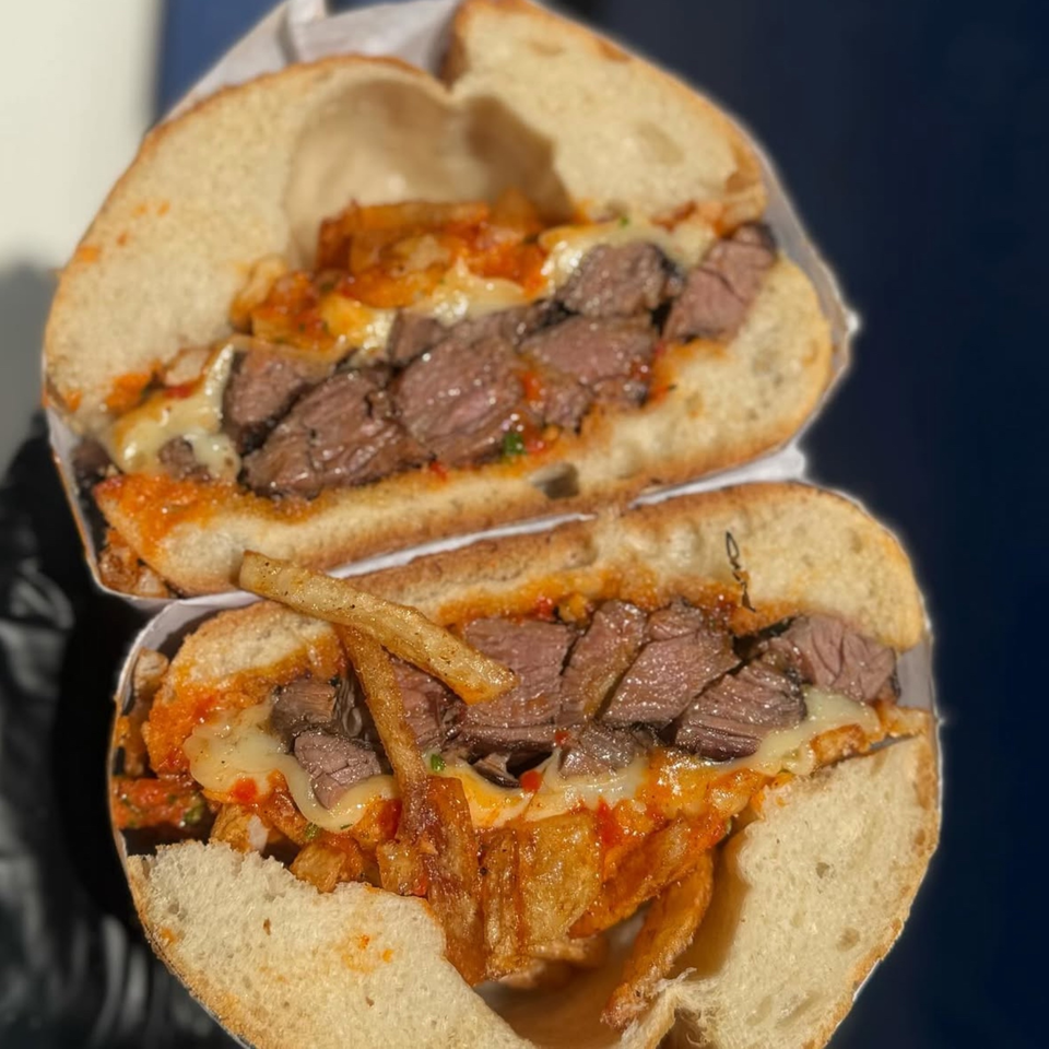 A sliced Emma's Deli steak sandwich with melted cheese, sauce, and fries inside.