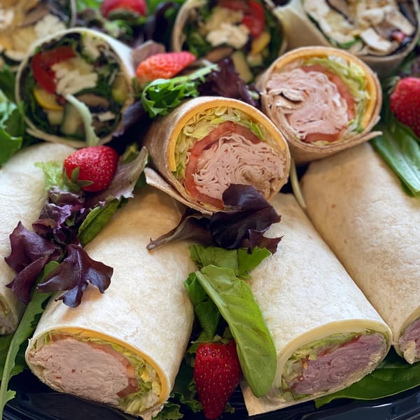 A platter of Emma's Deli wraps, filled with turkey, cheese, lettuce, and tomatoes, garnished with strawberries.
