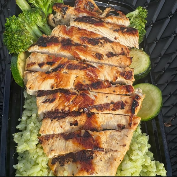 Grilled chicken slices with broccoli, zucchini, and green rice in a black container from Emma's Deli.
